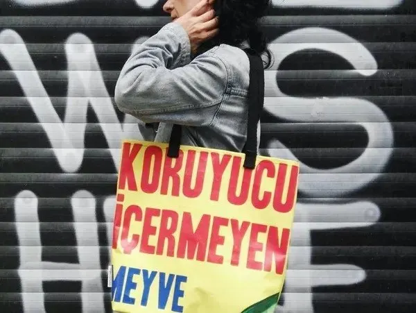 Grafiti duvarı önünde baskılı bir çantayı taşıyan kişi